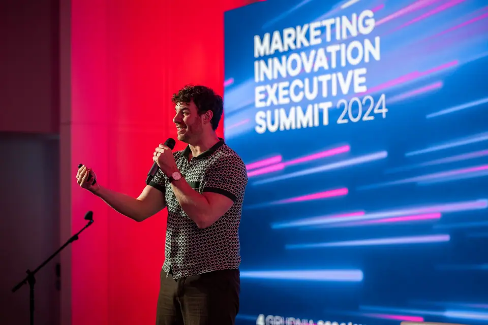 Prelegent z mikrofonem w energicznym geście na tle ekranu Marketing Innovation Executive Summit 2024